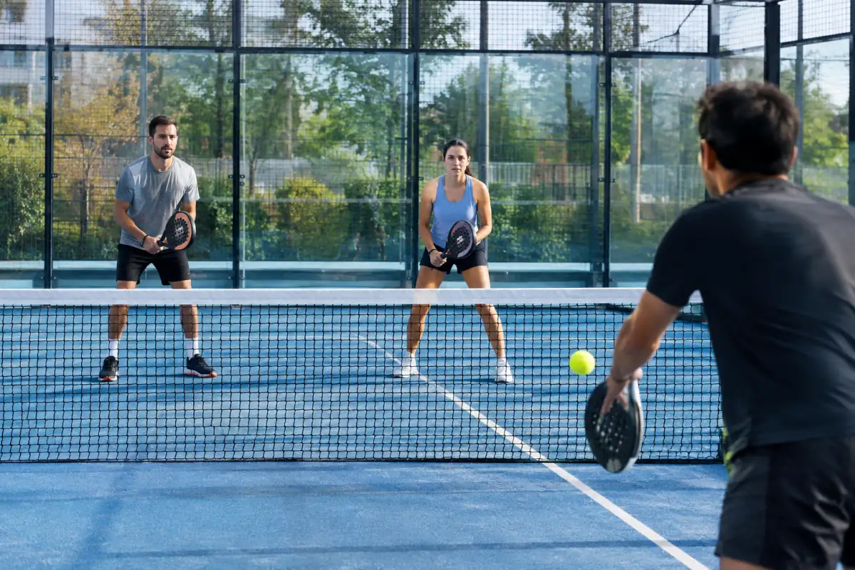 Deux partenaires s’entraînent à se déplacer ensemble au filet sur un terrain de padel vitré.