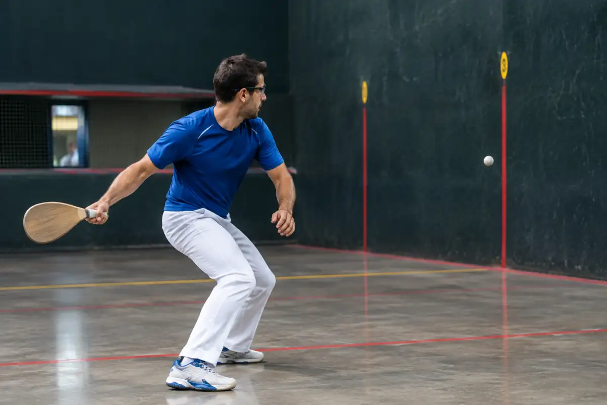 Joueur frappant une balle avec une pala en bois sur le frontis d’un fronton couvert de pelote basque.