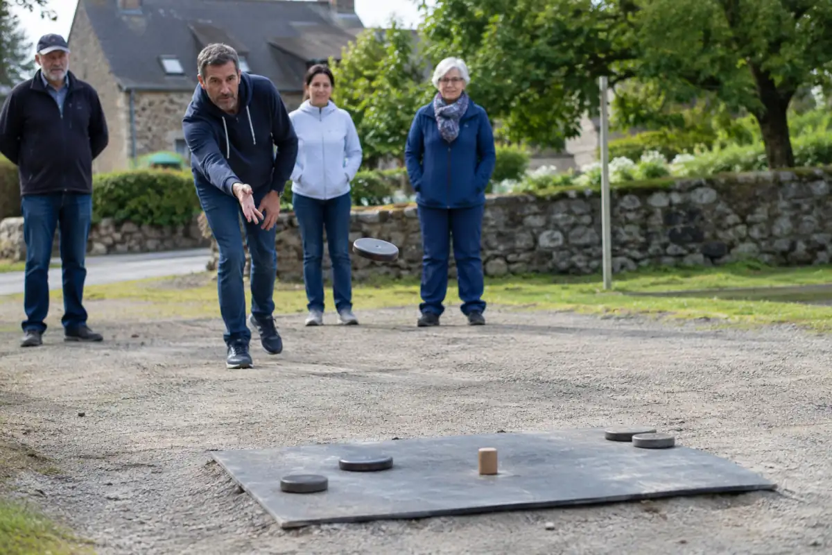 Joueur lançant un palet métallique vers le maître sur une planche de plomb lors d’une partie de palet breton en extérieur.