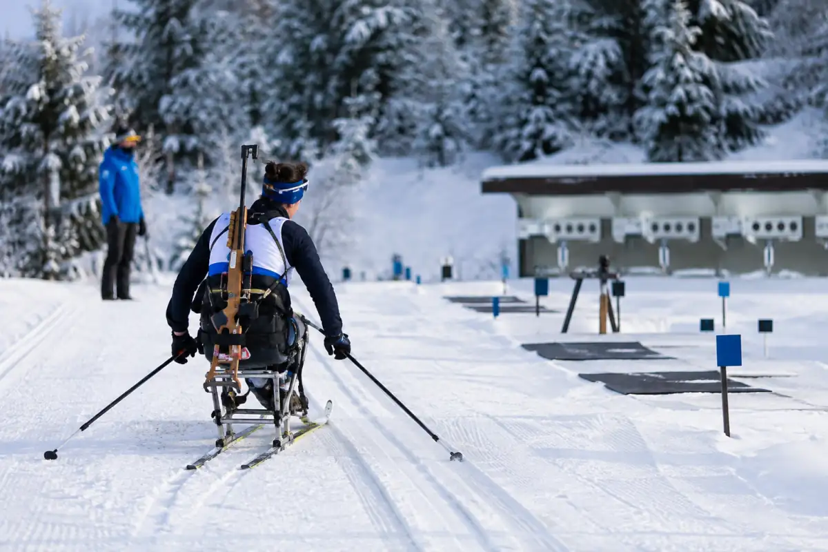 Un athlète en sit-ski progresse sur une piste enneigée de para biathlon avant le passage au pas de tir.