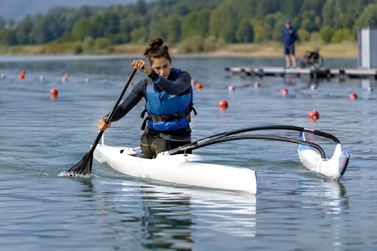 Athlète de para-canoë en va’a sur un plan d’eau calme, avec pagaie à une pale, flotteur latéral et assise adaptée.