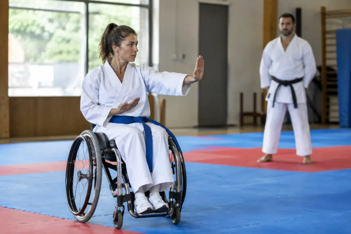 Athlète en fauteuil exécutant un kata de para-karaté dans un dojo accessible, sous le regard attentif d’un entraîneur.