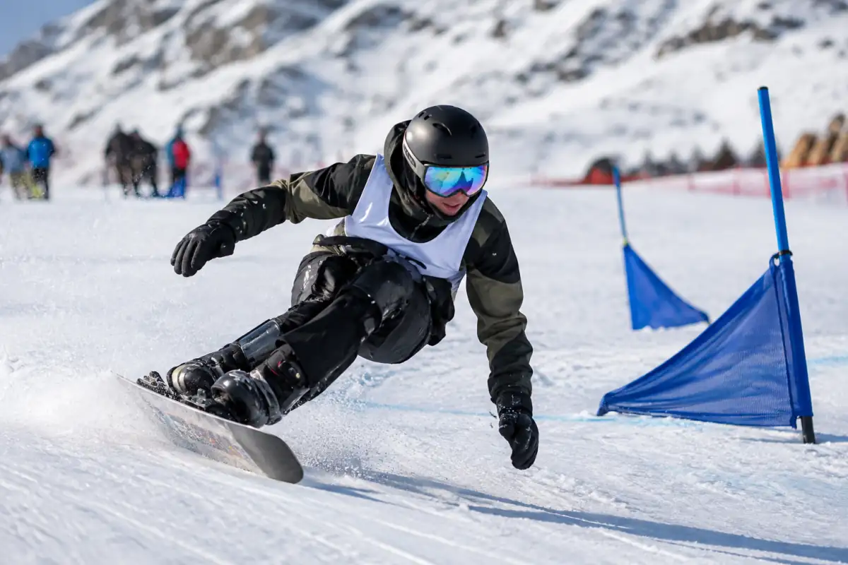 Une athlète en para snowboard négocie un virage relevé sur une piste enneigée, casque et protections visibles.