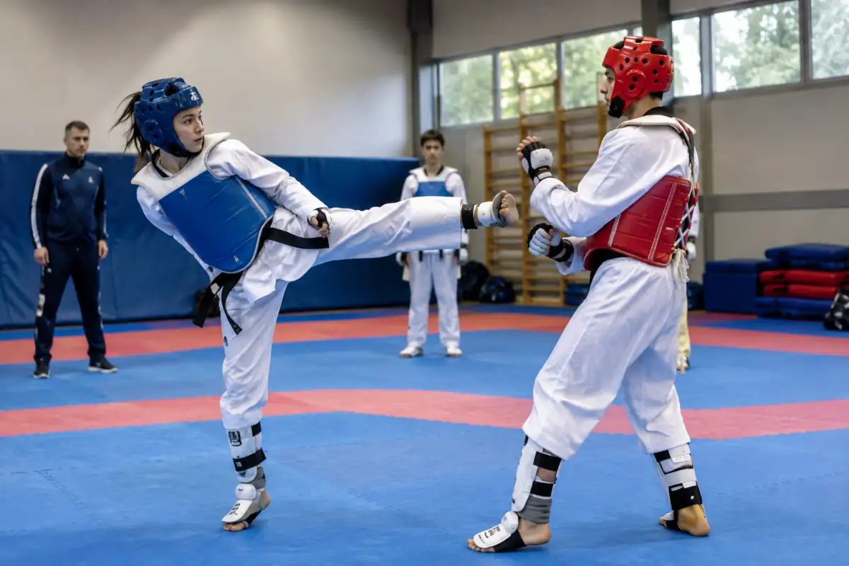Deux athlètes s’entraînent au para-taekwondo en salle, avec protections, lors d’un coup de pied contrôlé vers le plastron.