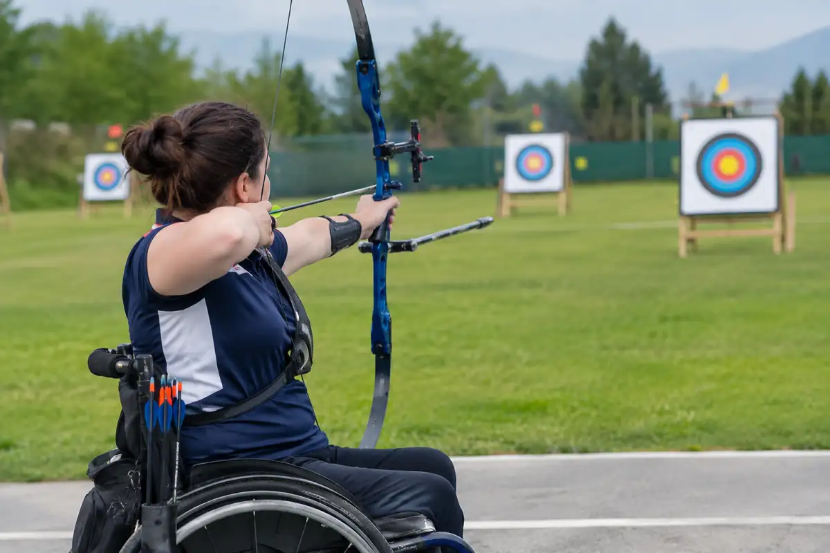 Archer en fauteuil visant une cible avec un arc classique lors d’une séance de para-tir à l’arc en extérieur.