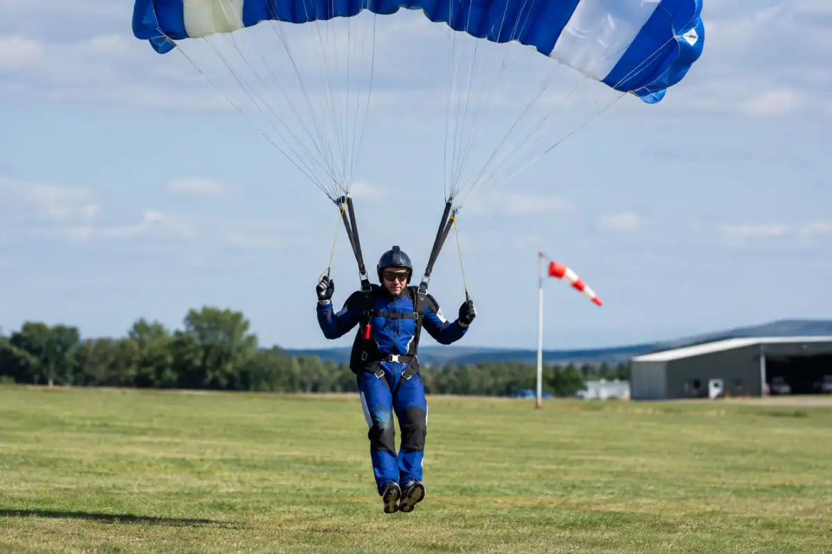 Un parachutiste pilote sa voile rectangulaire en approche d’atterrissage sur une zone herbeuse en France.
