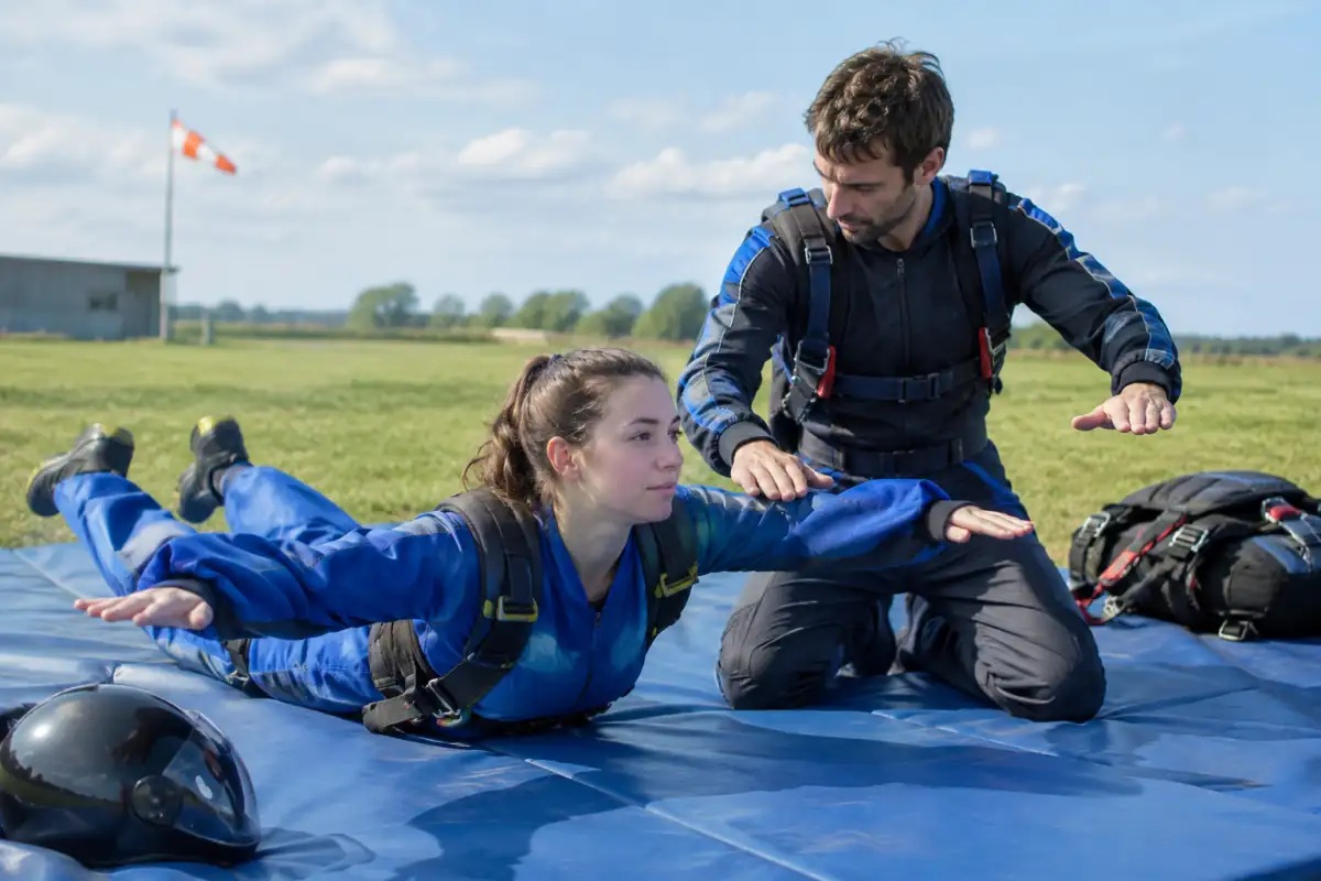 Un moniteur montre à une débutante la position de stabilité à répéter au sol avant une formation de parachutisme solo.