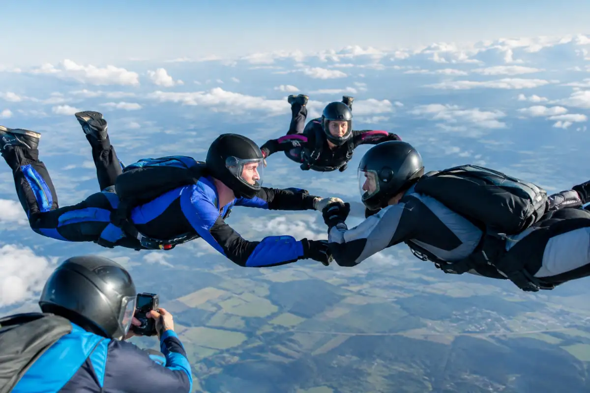 Parachutistes expérimentés construisant une formation de vol relatif en chute libre, filmés par un cadreur au-dessus des nuages.