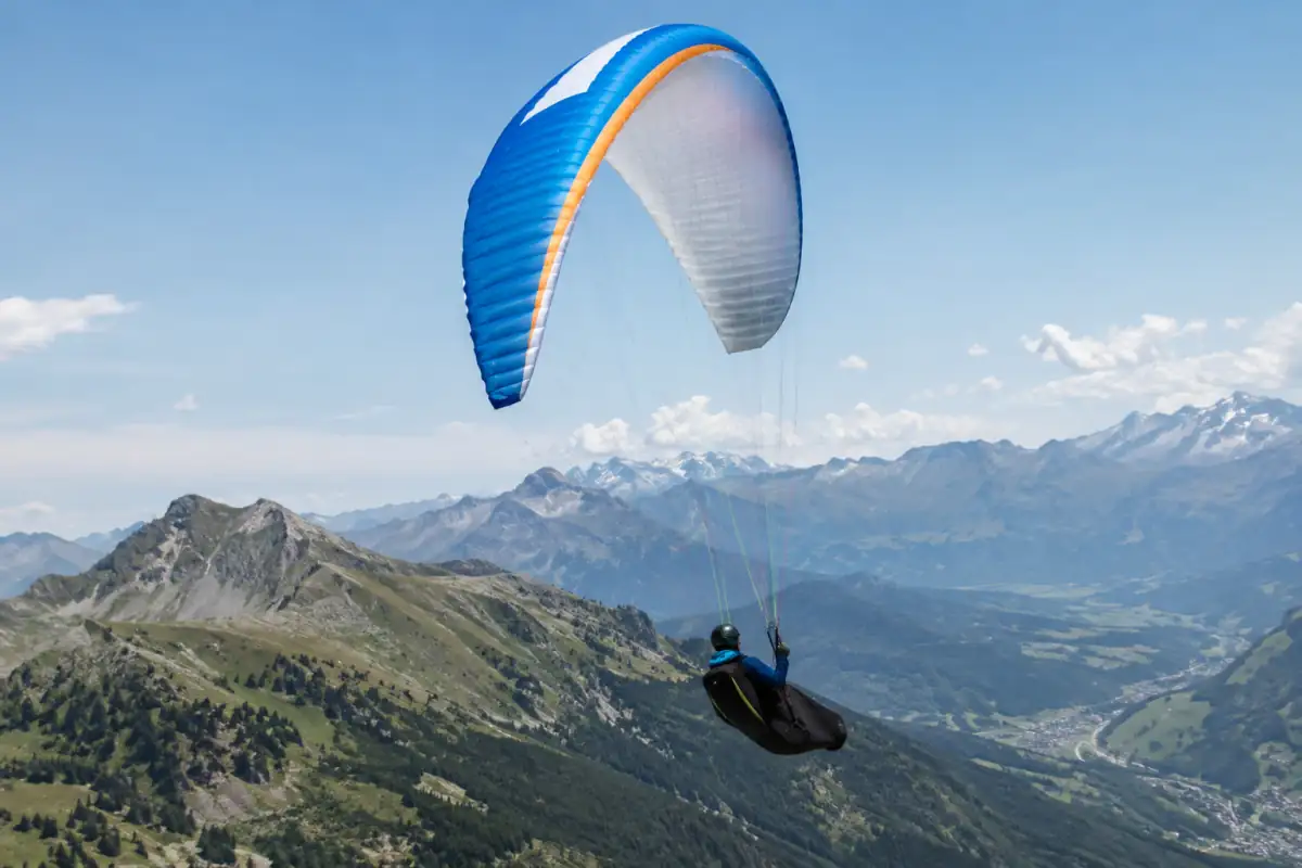Pilote de parapente de distance en vol sous son aile, exploitant une ascendance au-dessus d’un relief alpin français.