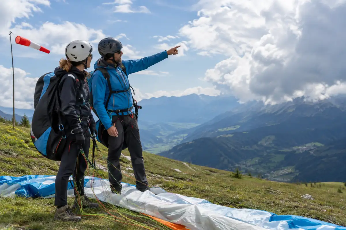 Un pilote débutant observe la manche à air et les nuages avec son encadrant avant un vol en parapente en montagne.