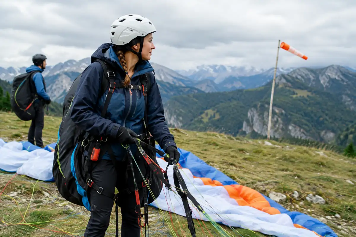Pilote débutant vérifiant les suspentes et les élévateurs de son parapente avant le décollage sur un site de montagne.