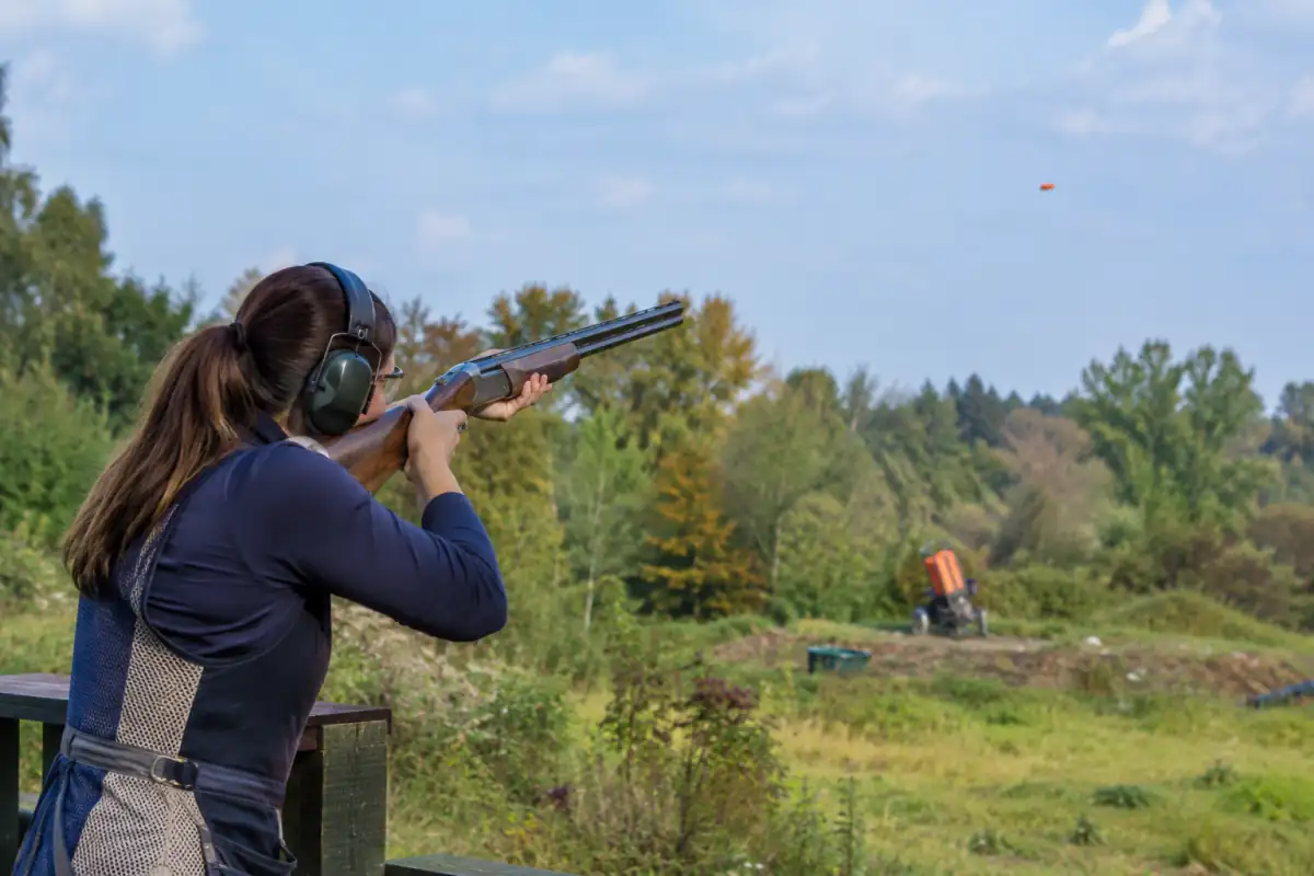 Tireur équipé de lunettes et d’un casque de protection suivant un plateau lancé sur un parcours de chasse en plein air.