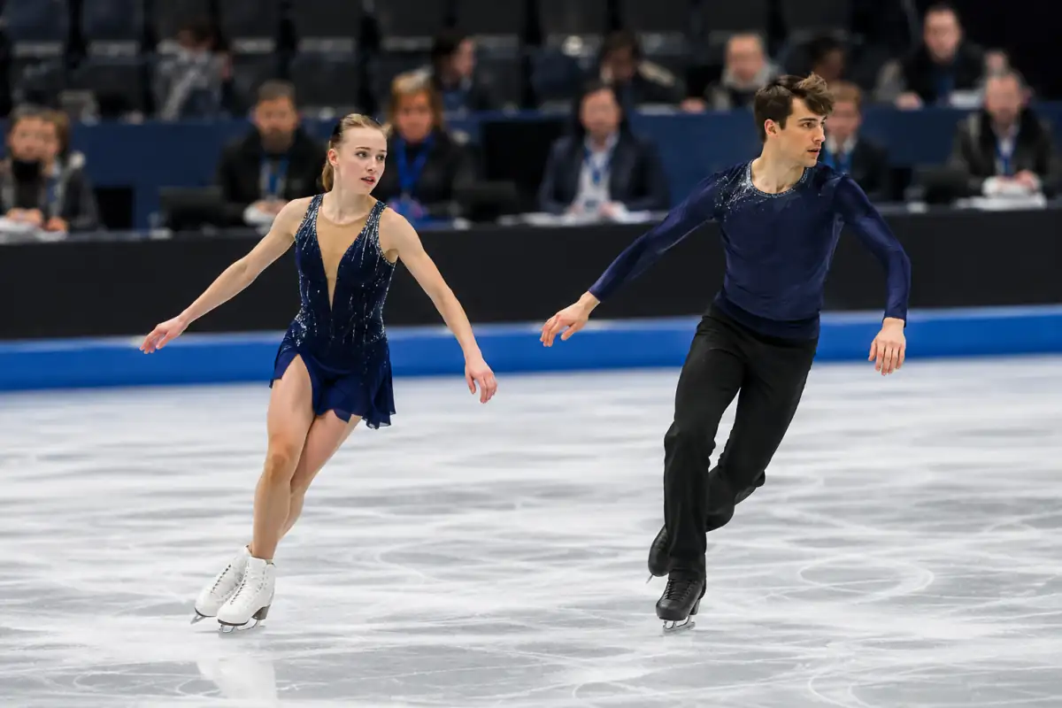 Un couple de patineurs termine un saut synchronisé en compétition, illustrant l’exécution technique évaluée par le jury.