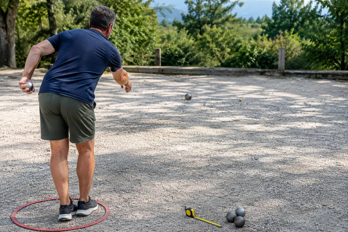 Joueur de pétanque dans un cercle d’entraînement, visant un but sur gravier avec des boules et un mètre à proximité.