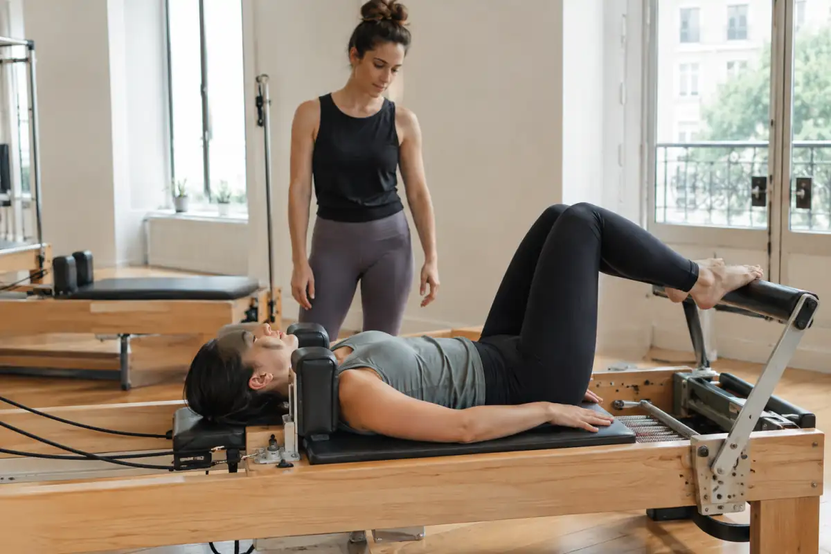 Une pratiquante réalise un exercice de poussée des jambes sur le chariot d’un reformer dans un studio de Pilates.