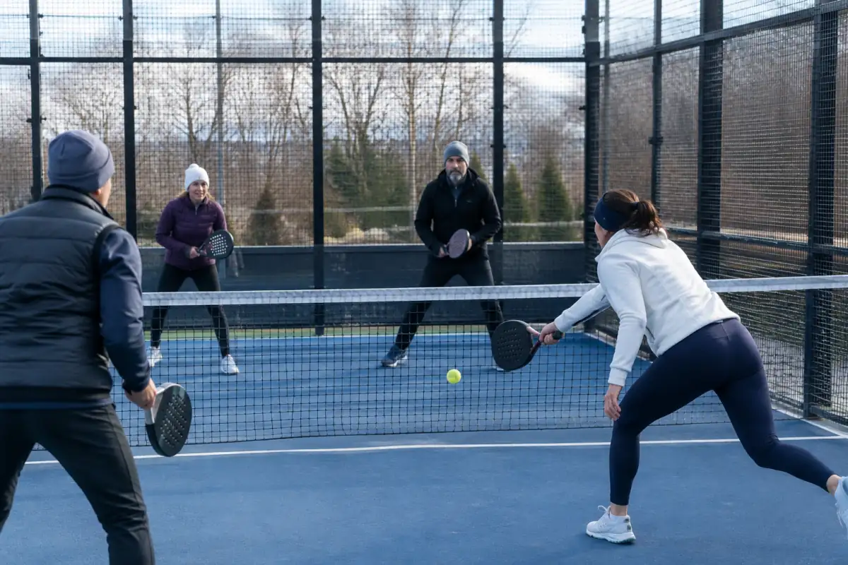 Échange de platform tennis en double sur une plateforme grillagée, avec raquettes pleines perforées et rebond de balle.