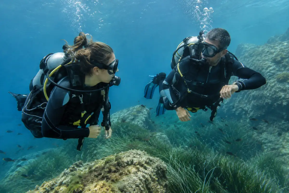 Deux plongeurs en scaphandre contrôlent leur flottabilité et leur ordinateur au-dessus d’un fond rocheux en Méditerranée.