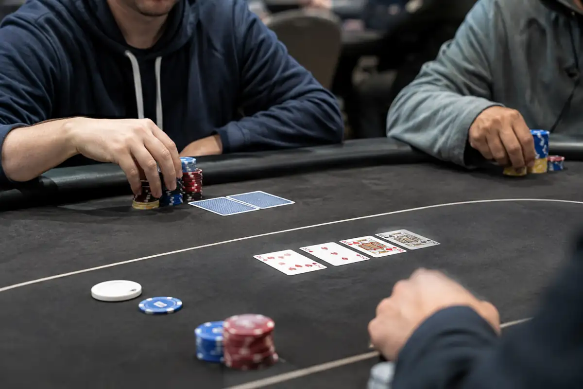 Un joueur organise son tapis près de ses cartes privées, du flop, du bouton et des blindes sur une table de tournoi.