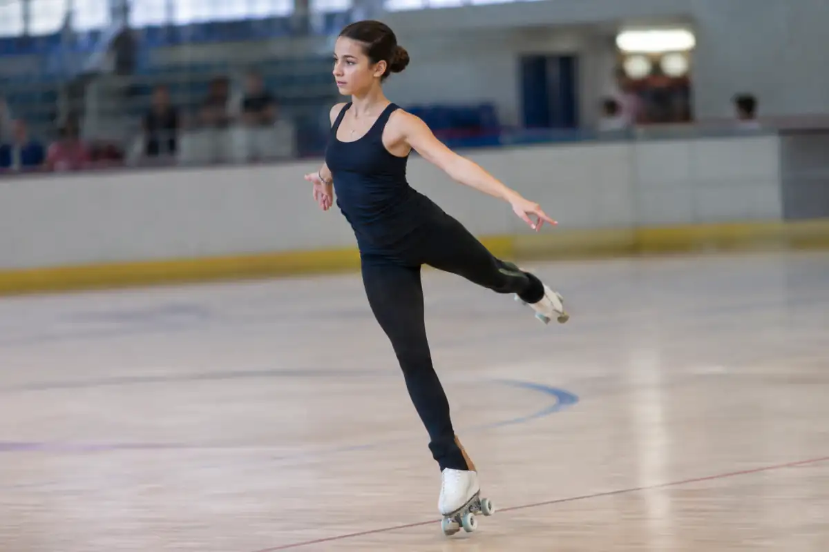 Patineuse réalisant une pirouette en roller artistique sur une piste intérieure, chaussée de patins à quatre roues.
