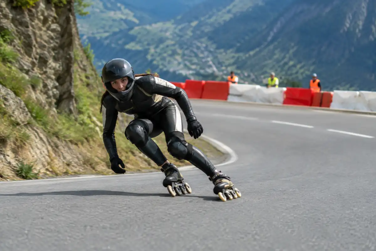 Patineur en roller de descente négociant un virage sur une route fermée, avec casque intégral et protections complètes.
