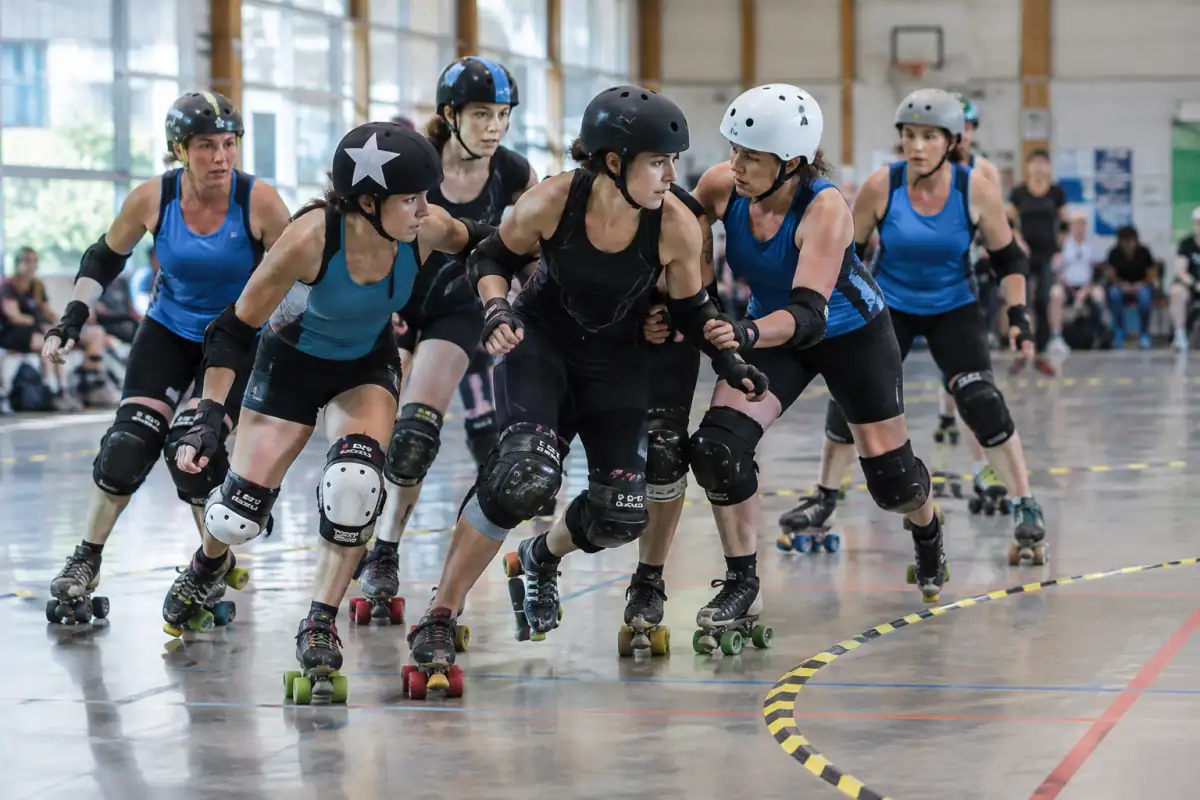 Une jammer en couvre-casque étoilé tente de dépasser le pack adverse lors d’un match de roller derby en salle.