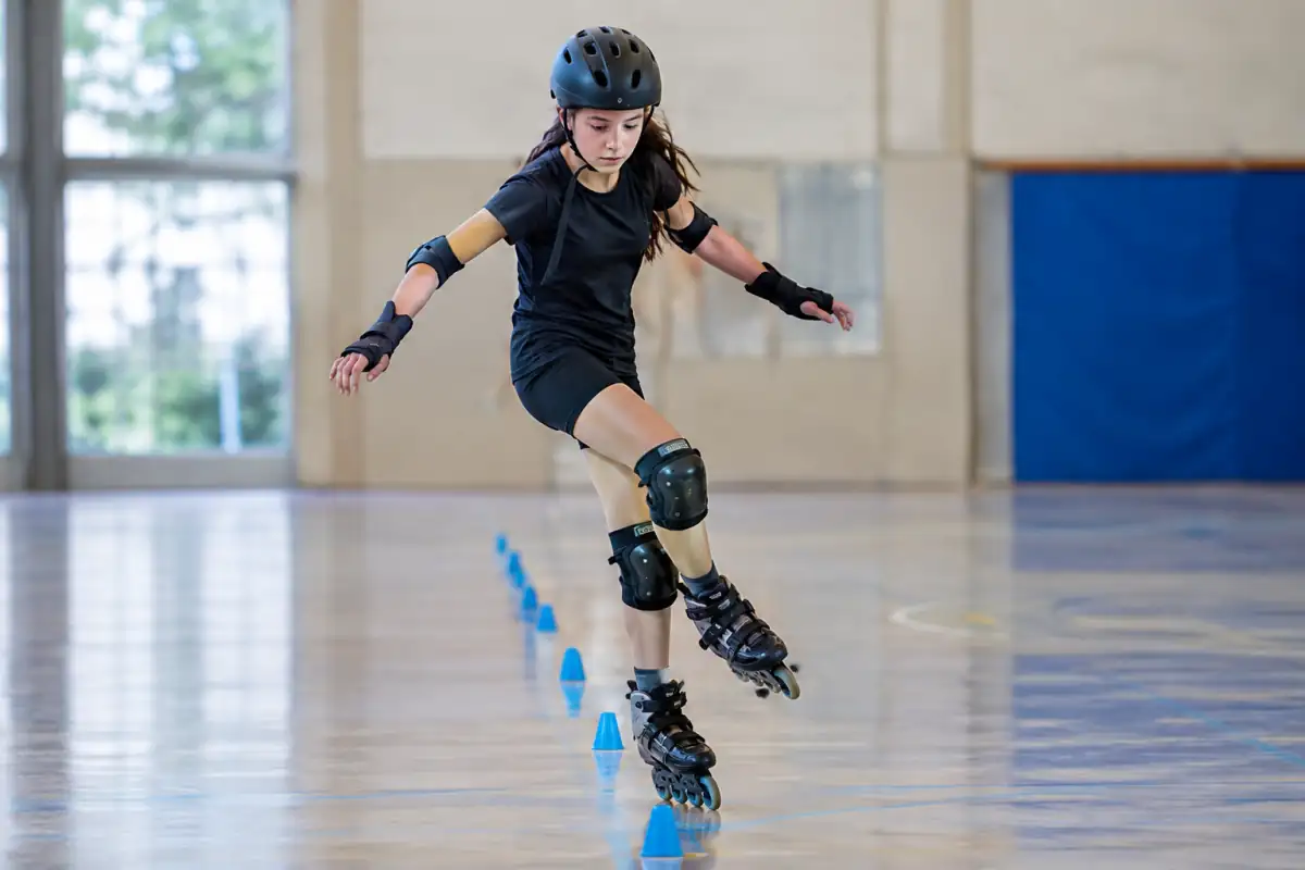 Patineur en rollers slalomant rapidement entre des plots alignés dans une salle, en équilibre sur un pied et protégé.