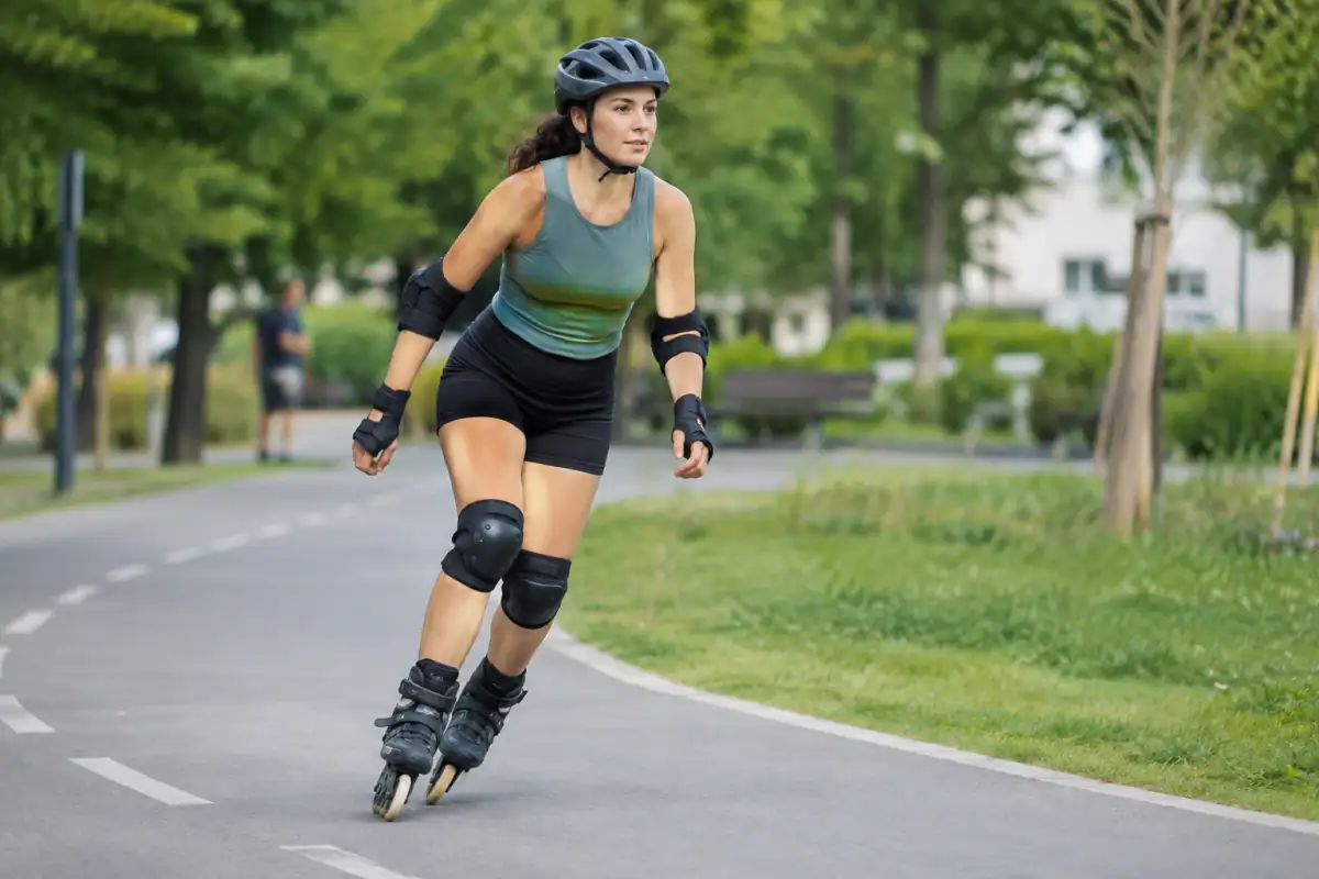 Une patineuse en roller en ligne, équipée d’un casque et de protections, glisse sur une piste cyclable sèche en parc.