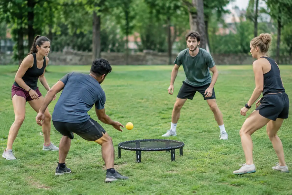 Deux équipes de deux joueurs disputent un échange de roundnet autour d’un petit filet circulaire posé sur l’herbe.