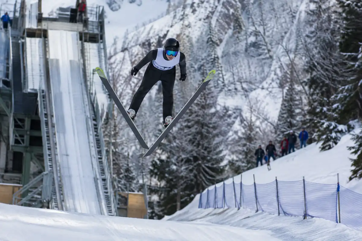 Sauteur à ski en position de vol en V au-dessus de la piste de réception d’un tremplin enneigé.