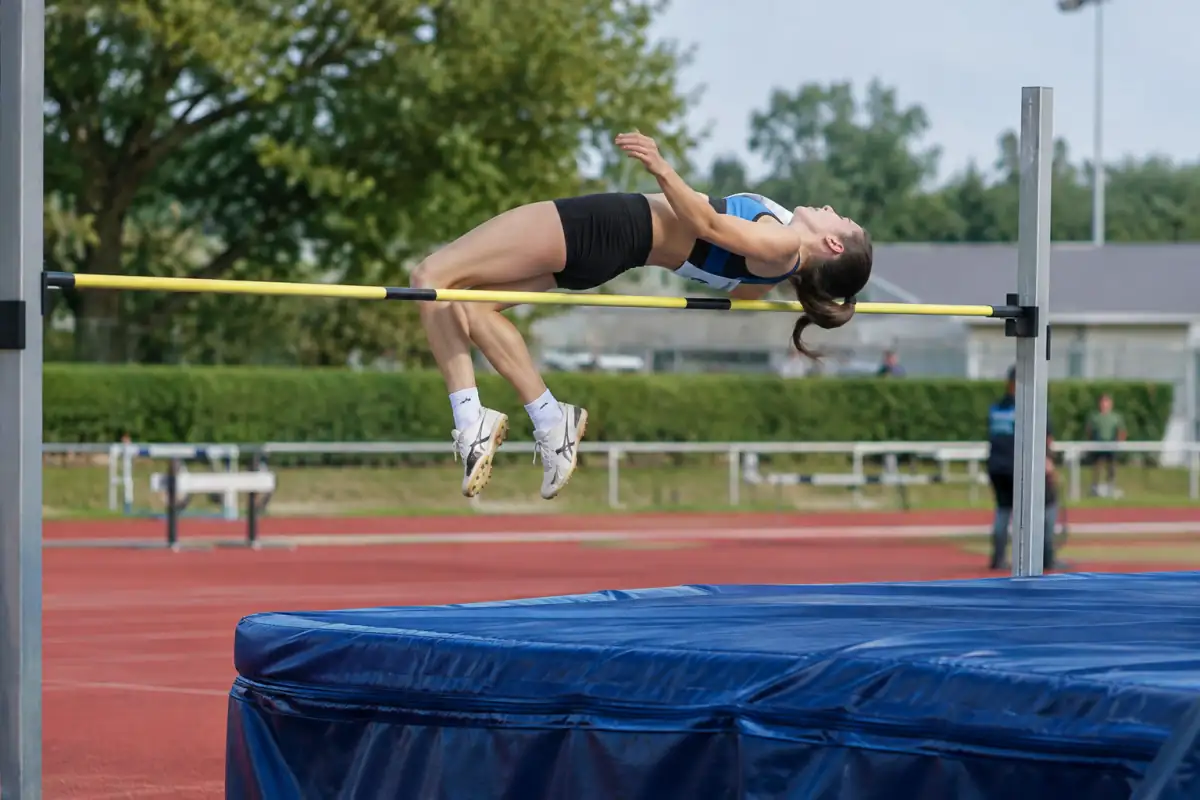 Athlète en plein Fosbury au-dessus de la barre lors d’une séance de saut en hauteur sur une piste d’athlétisme.