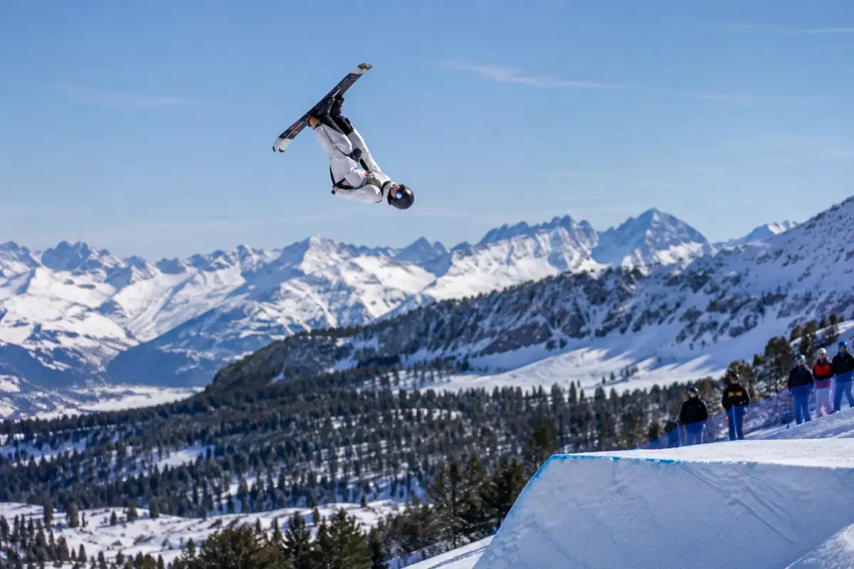 Un skieur de sauts acrobatiques à ski réalise un salto au-dessus d’un tremplin enneigé, avant la réception sur une piste raide.