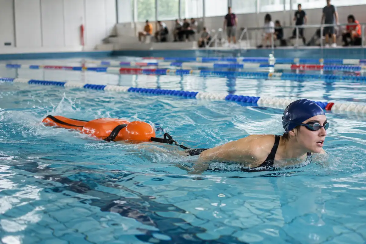 Athlète en palmes remorquant un mannequin avec un tube pendant une épreuve de sauvetage sportif en piscine.