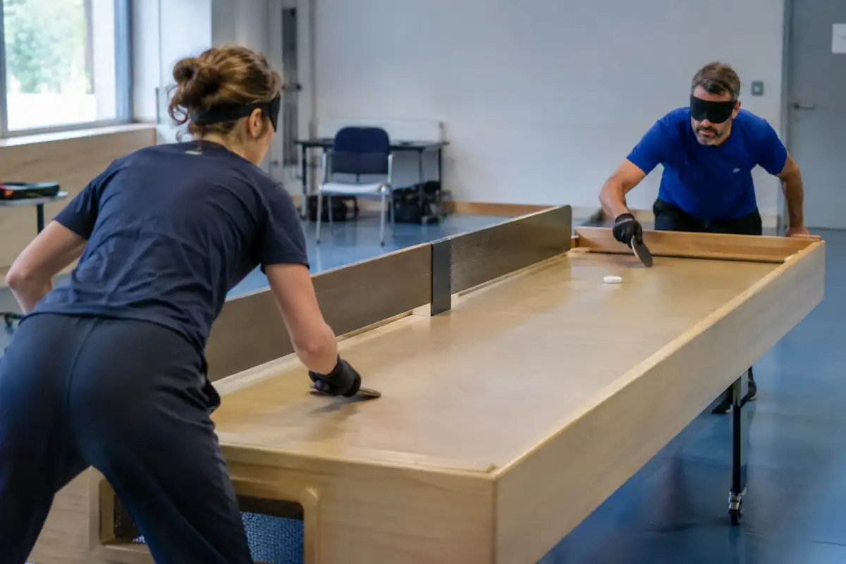 Deux joueurs masqués disputent un échange de showdown autour d’une table à rebords avec raquettes et palet sonore.