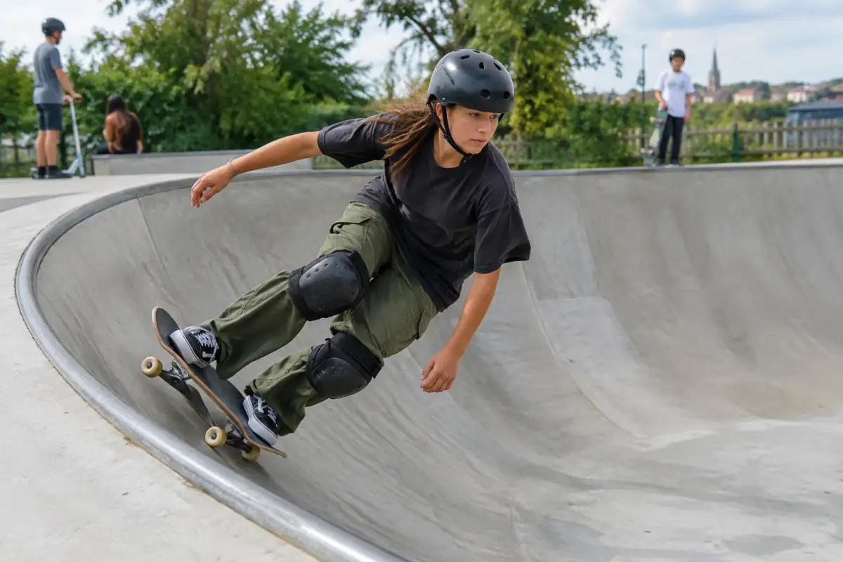 Skateur casqué enchaînant une courbe sur la transition en béton d’un skatepark, avec genouillères et planche adaptée.