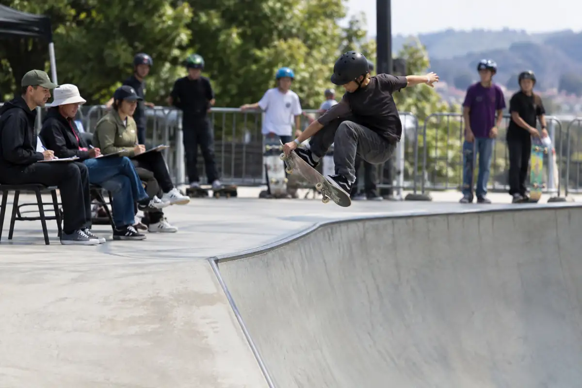 Un rider exécute une figure dans un bowl pendant que les juges observent son run et que les autres participants attendent leur tour.