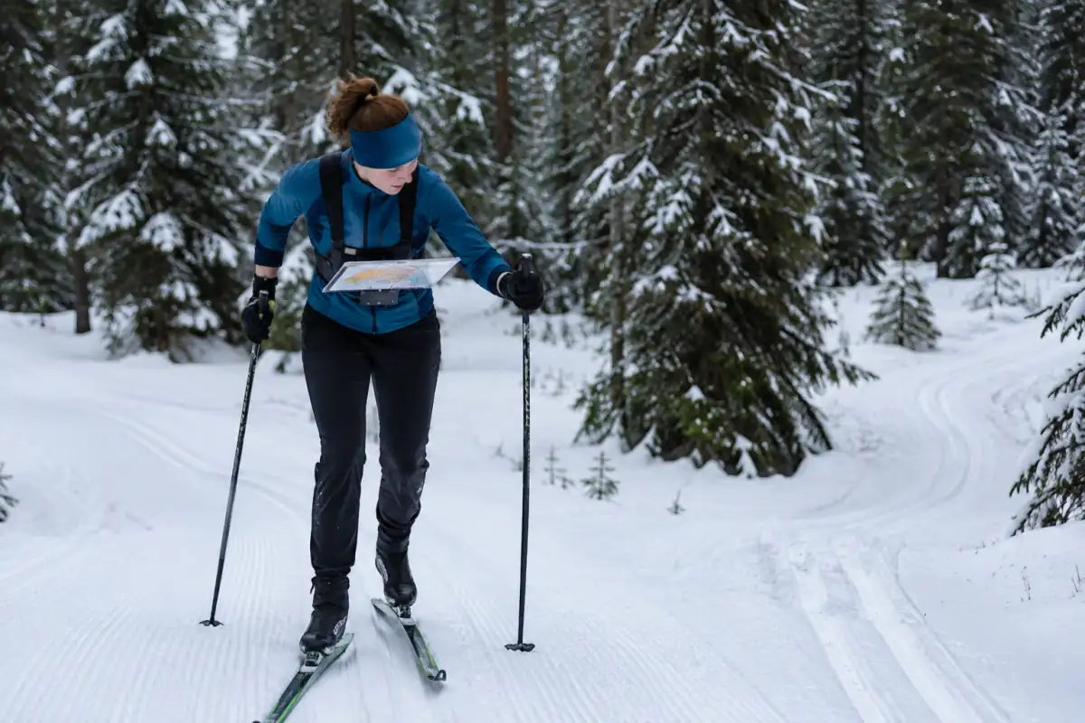 Un skieur consulte sa carte sur un porte-carte de poitrine en approchant d’un carrefour lors d’une course de ski d’orientation.