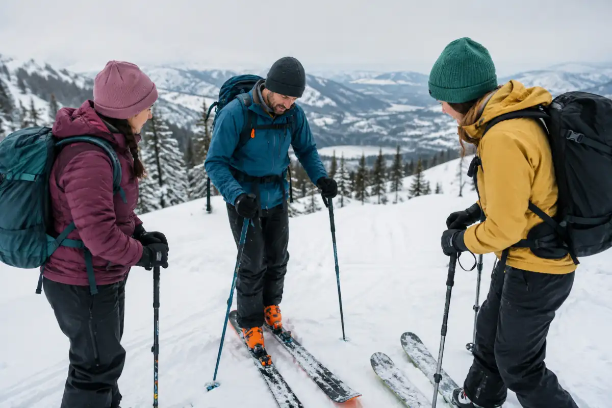 Un guide explique l’itinéraire à deux débutants équipés de skis de randonnée sur une pente douce en montagne.