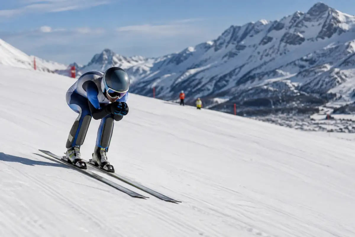 Un skieur en position aérodynamique accélère sur une piste dédiée au ski de vitesse dans les Alpes françaises.