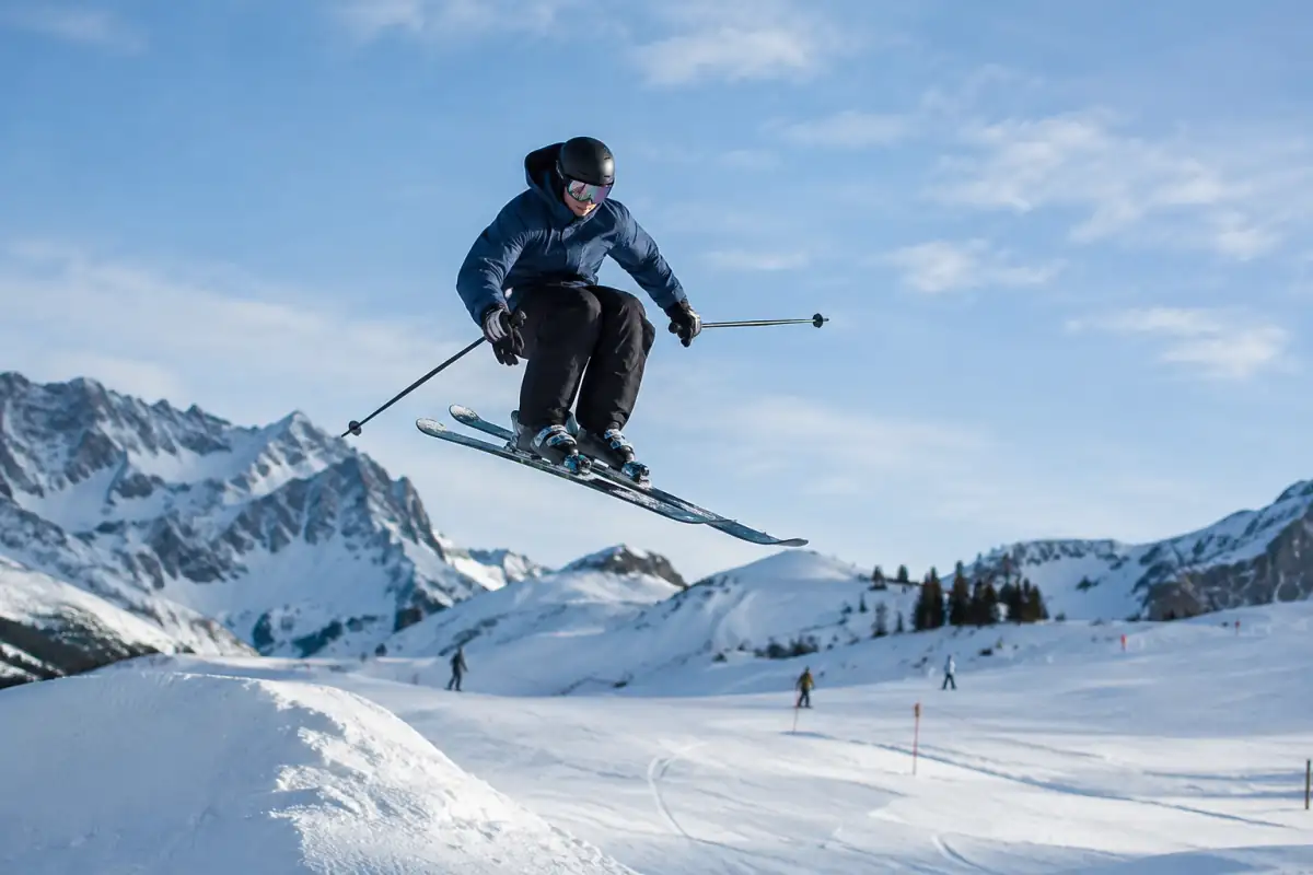 Un skieur en casque réalise un petit saut maîtrisé sur un module enneigé de ski freestyle dans une station alpine.