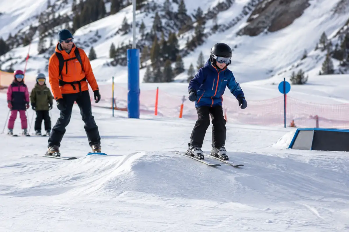 Un moniteur accompagne des débutants sur un relief bas, dans une zone d’initiation dégagée en bord de snowpark.