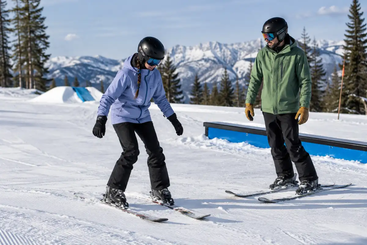 Débutant en ski freestyle travaillant sa position fléchie sur une piste facile, avec un encadrant à proximité.