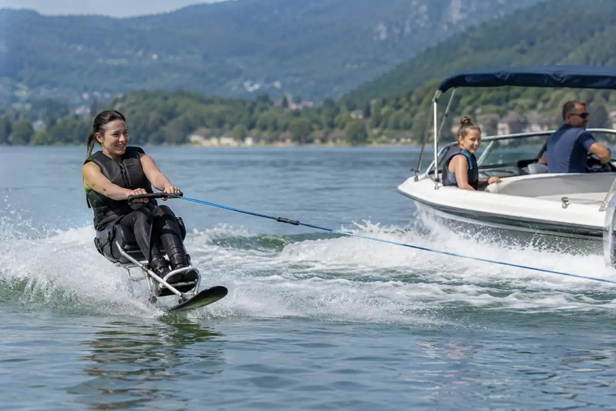 Ski nautique adapté : un sportif assis sur un sit-ski glisse derrière un bateau, équipé d’un gilet de flottabilité.