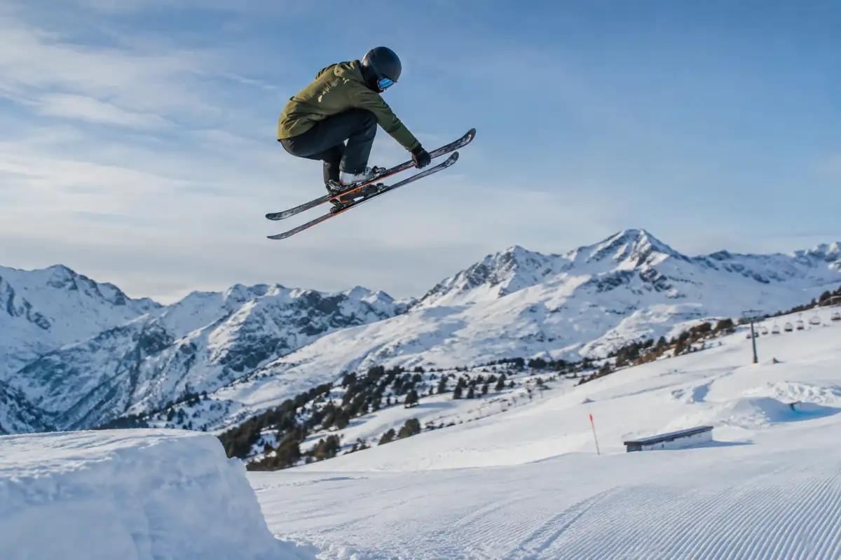 Skieur en casque réalisant une figure au-dessus d’un saut aménagé dans un snowpark de ski slopestyle.
