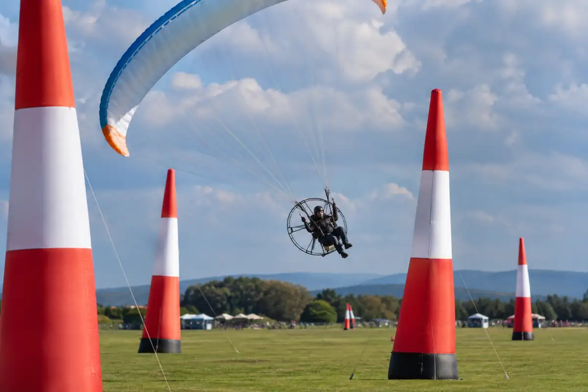 Un pilote de slalom paramoteur négocie un virage entre des pylônes gonflables sur un terrain dégagé.