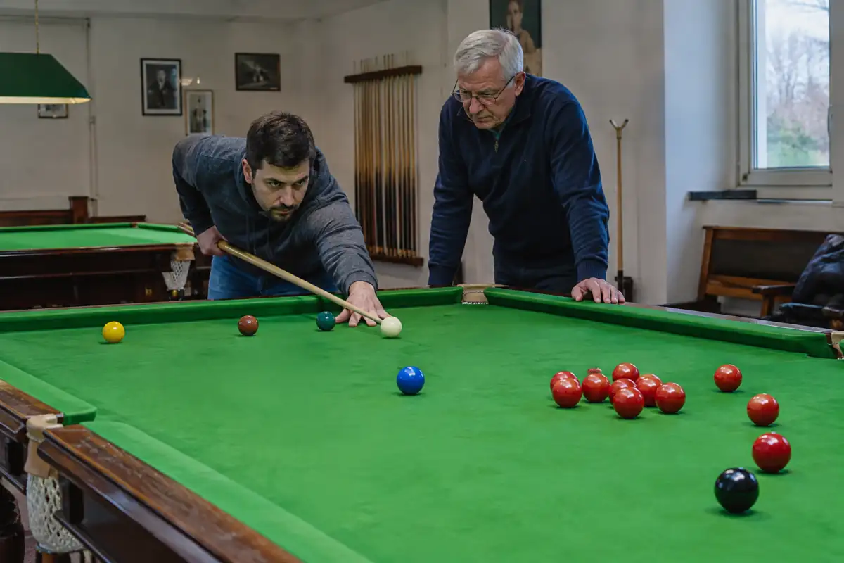 Un débutant travaille son geste à la queue sur une table de snooker, accompagné par un membre du club.