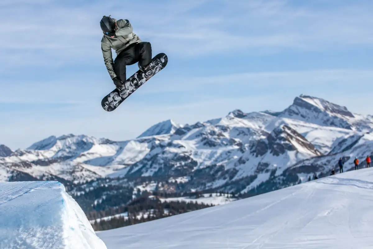 Snowboardeur casqué réalisant une figure en big air au-dessus d’un module aménagé dans un snowpark alpin.