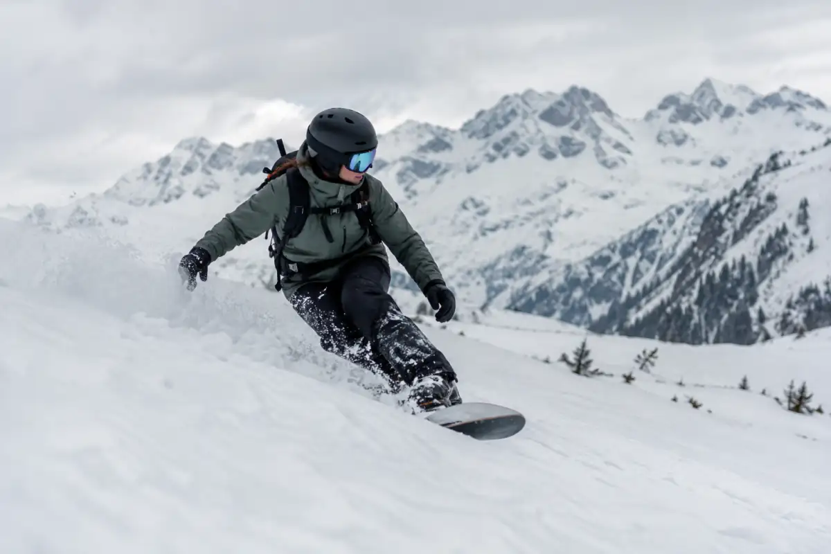 Snowboardeur en virage contrôlé dans une pente naturelle enneigée, équipé d’un casque et d’un sac de sécurité avalanche.