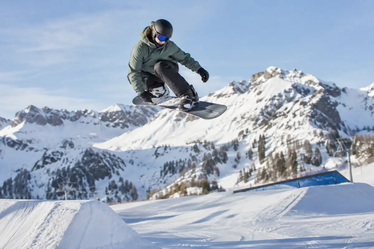 Un snowboardeur réalise un grab sur un saut aménagé dans un snowpark, en pleine session de snowboard slopestyle.
