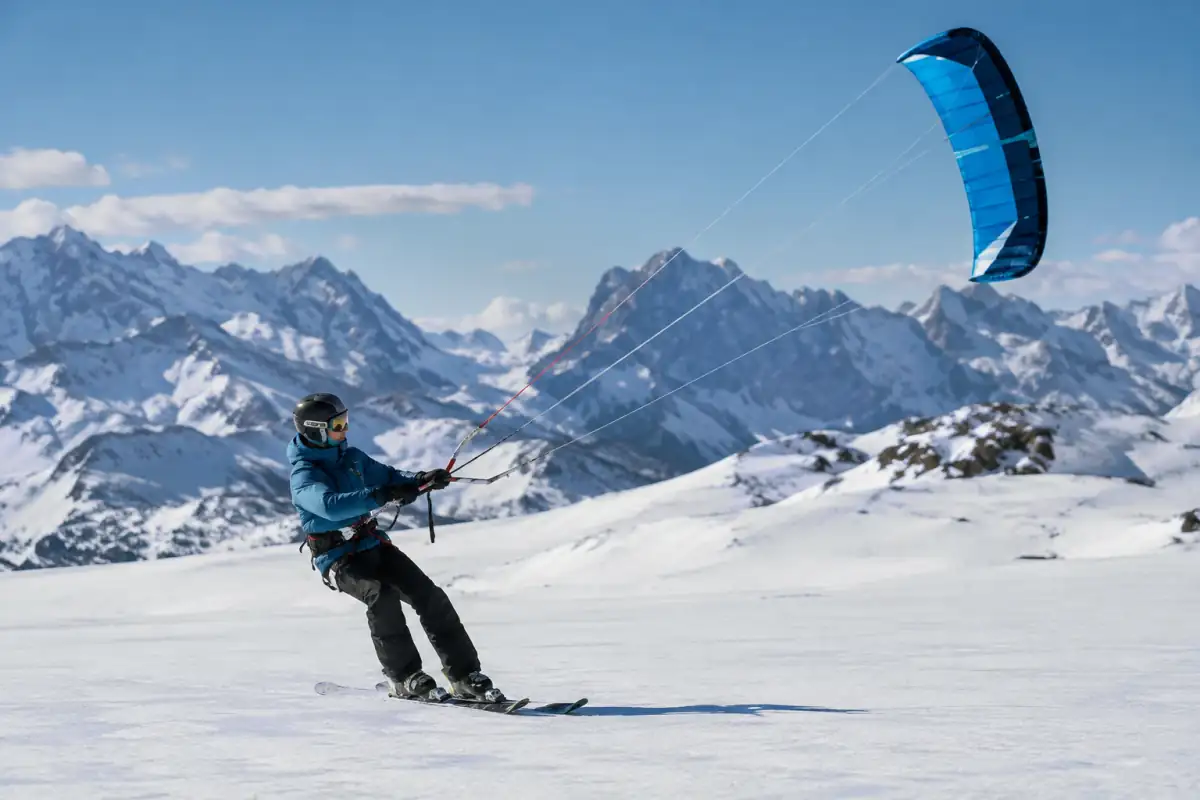 Un pratiquant de snowkite glisse à skis sur un plateau enneigé des Alpes, tracté par une aile de traction.
