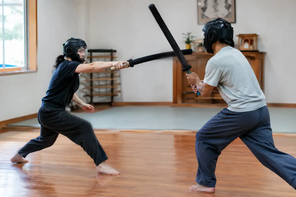Deux pratiquants de sport chanbara en assaut contrôlé, casques de protection et armes souples dans un dojo.
